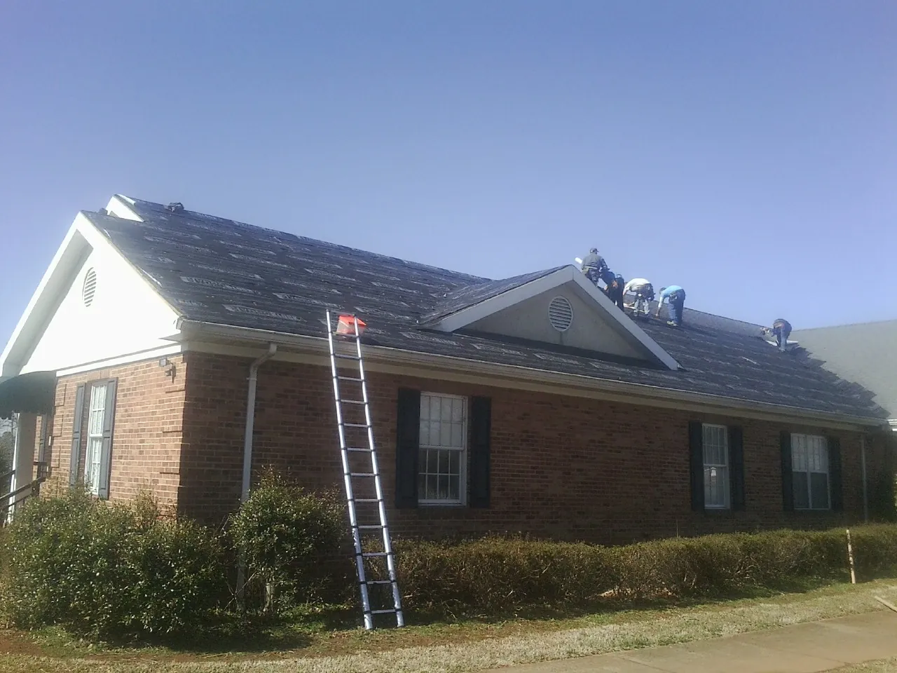 Crew tearing shingles off a brick ranch roof with a ladder set — Emergency Roof Repair work by our crew in Collins