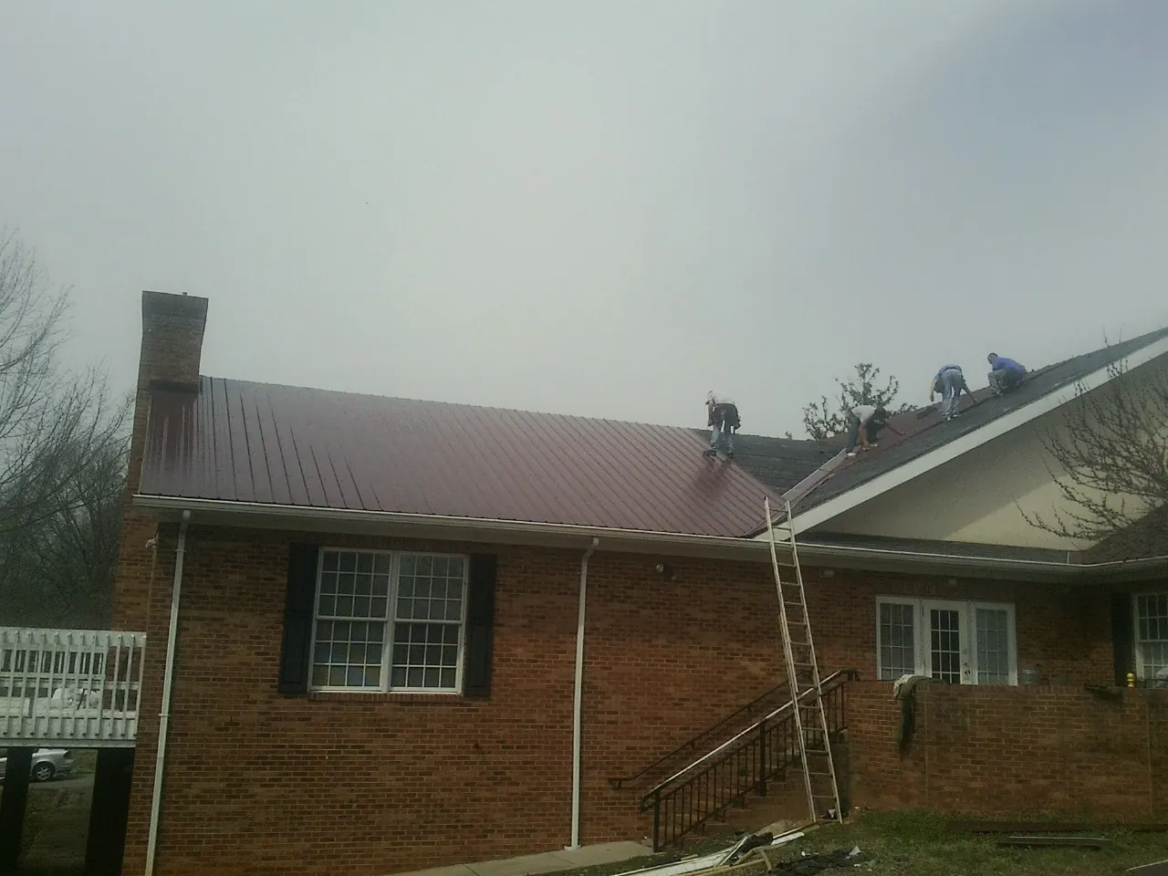Crew setting red metal roofing panels on a brick home in Collins