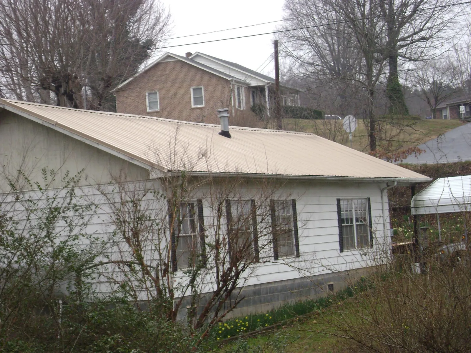 Tan metal roof on a white sided house set into a hillside — Commercial Roofing by Roofing Brothers in Collins
